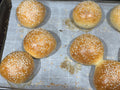 Fresh baked sesame sourdough hamburger buns on a sheet pan
