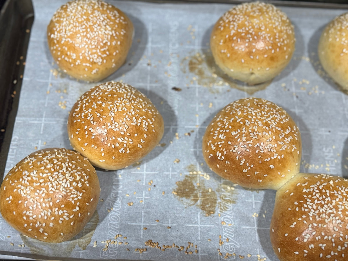 Fresh baked sesame sourdough hamburger buns on a sheet pan